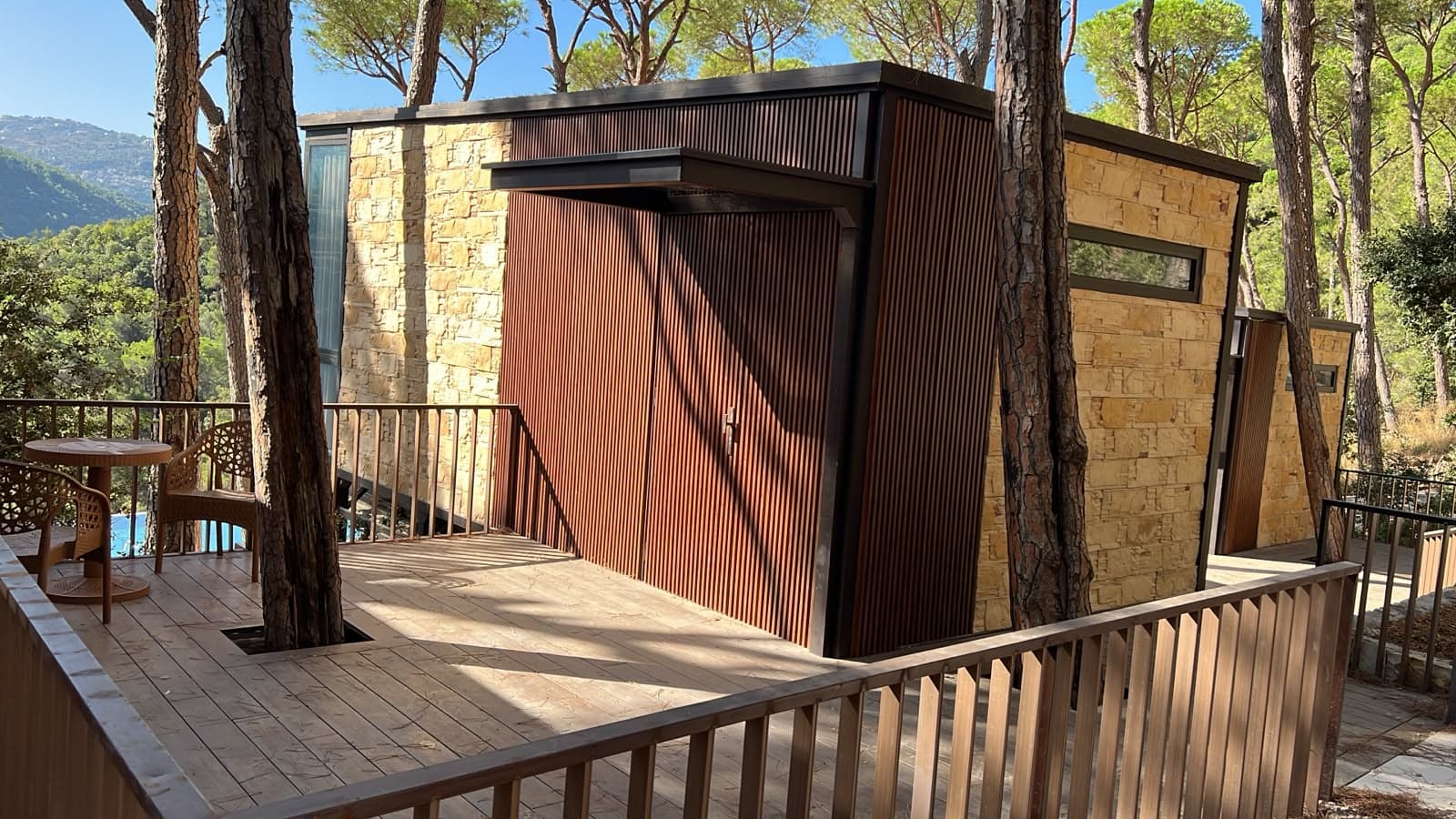 Pinea Luna, stone and timber-slatted walls on a deck built around the pines, with the pool and the valley below